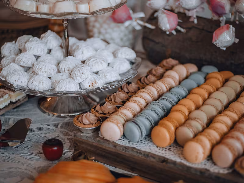 Mesa de postres gourmet con macarons y bocadillos individuales sobre bases escalonadas
