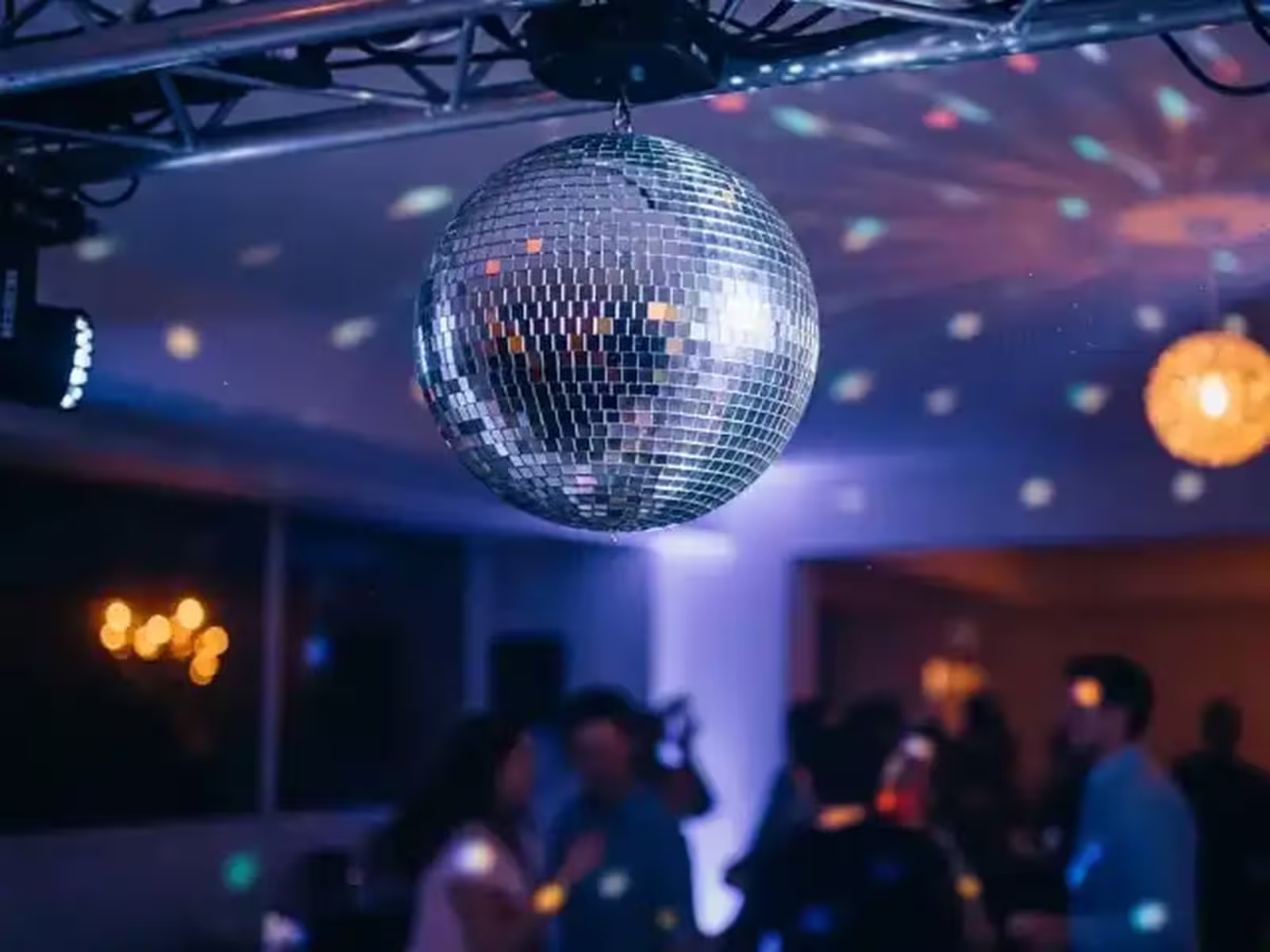Bola disco de espejos girando sobre una pista de baile con haces de luz reflejados en el salón