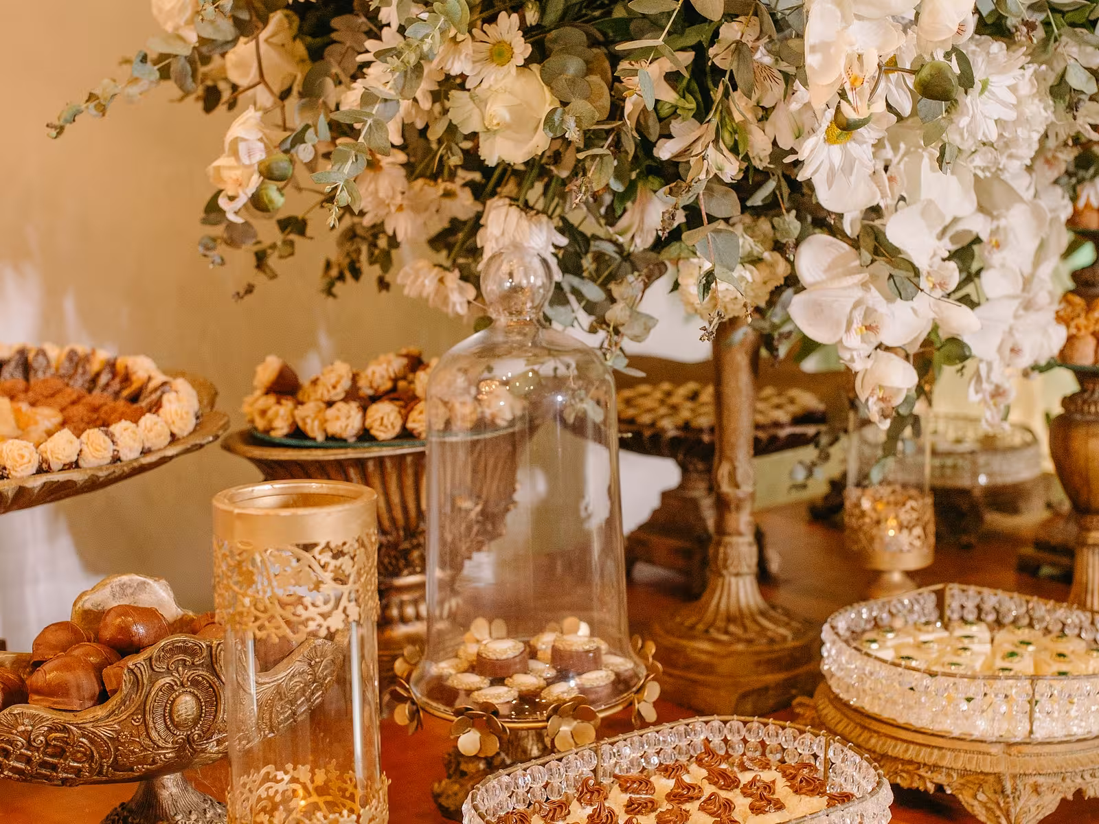 Mesa de dulces premium montada con base floral, campanas de cristal y bocadillos en un evento
